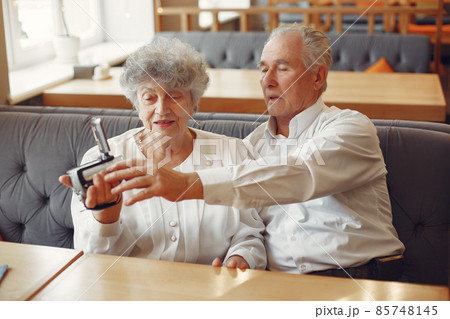 Elegant old couple in a cafe using a camera 85748145