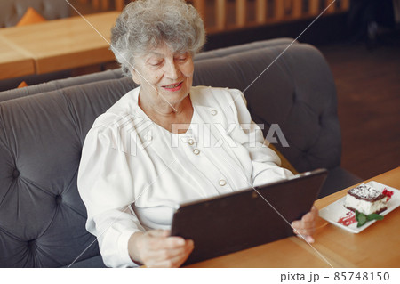 Elegant old woman sitting in a cafe and using a laptop 85748150