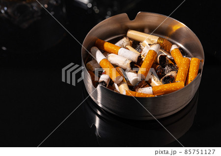 Ash tray full of cigarette butts on black background 85751127
