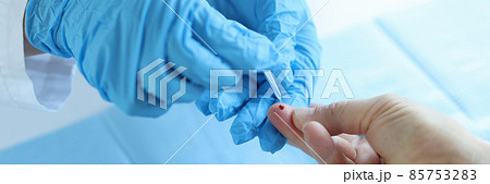 Doctor wearing disposable gloves takes blood from patient finger 85753283