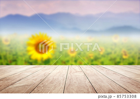 Wooden table top with blurry Sunflower field against mountains landscape 85753308