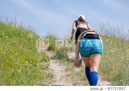 Tired sportswomen ascending hill on trail running contest Tired sportswomen ascending hill on trail running contest 85757087