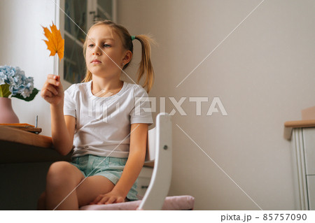 Low-angle view of little girl holding beautiful dried maple leaf to create herbarium diy at home. 85757090