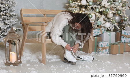 Young pretty woman wearing mittens lacing ice skates before skating Young pretty woman wearing mittens lacing ice skates before skating 85760960