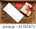 Wooden box with present wrapped in brown craft paper with red ribbon, with empty blank card 85762672