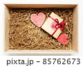 Wooden box with present wrapped in brown craft paper with red ribbon, filled with paper filler, top view 85762673