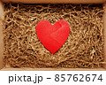 Present box with big red heart lying on brown shredded craft paper filler 85762674