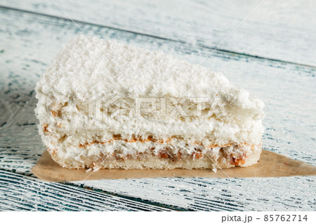 Piece of cake with white coconut chips on a wooden background. Old boards. 85762714