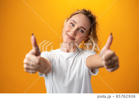 Young teen woman showing thumbs up sign against yellow background Young teen woman showing thumbs up sign against yellow background 85762936