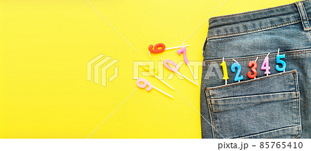 Burning birthday candles sticking out of the back pocket of blue jeans on yellow background Number 0-9 Burning birthday candles sticking out of the back pocket of blue jeans on yellow background Number 0-9 85765410