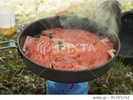 Close up of raw red trout fish fillet of freshly caught arctic char with green herbs, frying on cooking pan at camping gas cooker. Outdoor cooking. 85765742