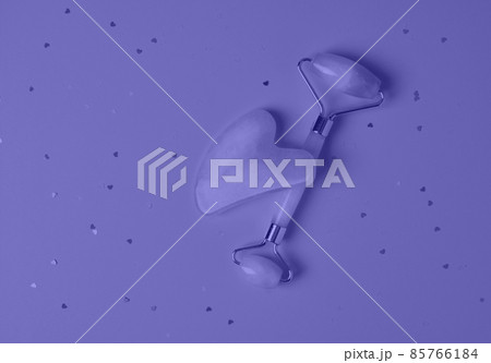 Roller and gua sha facial massage tools on a violet background with sparkles in the shape of hearts. Skin care, beauty and health concept. Color of the Year 2022 Roller and gua sha facial massage tools on a violet background with sparkles in the shape of hearts. Skin care, beauty and health concept. Color of the Year 2022 85766184