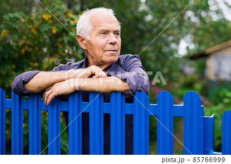 Portrait of gray-haired owner at fence of his country house in village Portrait of gray-haired owner at fence of his country house in village 85766999