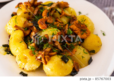 baked potatoes with chanterelles, served with herbs on white plate 85767003