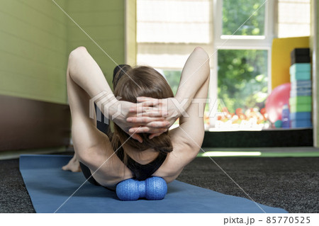 Girl lies on yoga mat and does back massage with roller for physiotherapy. Myofascial release with foam ball. Back view Girl lies on yoga mat and does back massage with roller for physiotherapy. Myofascial release with foam ball. Back view 85770525