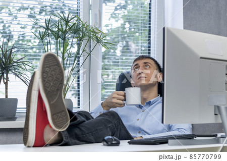 Lazy employee in office put his feet on desk and drinks coffee. Man in procrastination. Lunch time. Lazy employee in office put his feet on desk and drinks coffee. Man in procrastination. Lunch time. 85770799