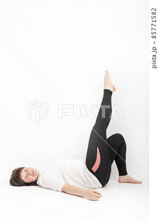 Curvy woman in sportswear holding doing exercise. Girl lies on back with her leg raised on white background. Vertical frame Curvy woman in sportswear holding doing exercise. Girl lies on back with her leg raised on white background. Vertical frame 85771582