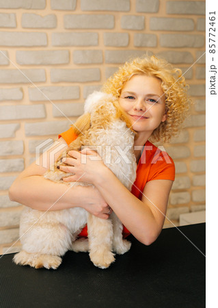 Vertical portrait of cheerful female groomer hugging curly Labradoodle dog after haircutting at grooming salon. Vertical portrait of cheerful female groomer hugging curly Labradoodle dog after haircutting at grooming salon. 85772461