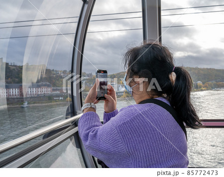 A middle-aged Asian woman with a smartphone wearing face mask in a cable car A middle-aged Asian woman with a smartphone wearing face mask in a cable car 85772473
