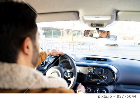 Man holding driving wheel riding car looking in rearview mirror at daytime 85775044