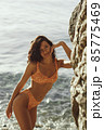 Beach Girl Model in Orange Bikini on the Rocky Deserted Seashore During Summer Beach Holidays 85775469