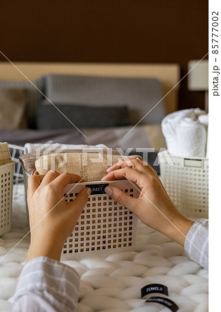 Woman hands neatly folded linens and towels use Marie Kondo method with sticky label tags 85777002