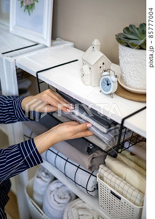 Domestic woman in pajamas neatly putting folded linens into cupboard vertical storage Marie Kondo 85777004