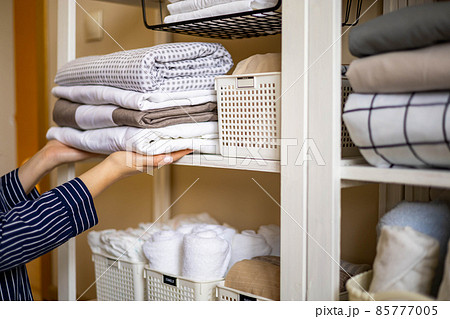 Domestic woman in pajamas neatly putting folded linens into cupboard vertical storage Marie Kondo 85777005
