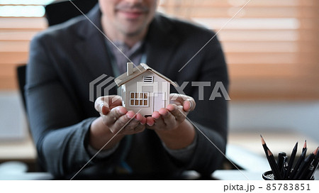 Real estate agent holding small house model. Mortgage and real estate investment concept. 85783851