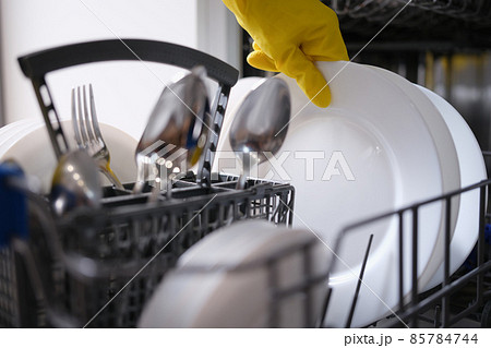 A hand in a yellow glove pulls dishes out of the dishwasher A hand in a yellow glove pulls dishes out of the dishwasher 85784744