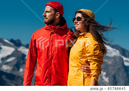 Portrait of travelers against the background of mountains. Portrait of travelers in tourist clothes in the mountains. A sporty couple on top of a mountain. An active couple is engaged in hiking Portrait of travelers against the background of mountains. Portrait of travelers in tourist clothes in the mountains. A sporty couple on top of a mountain. An active couple is engaged in hiking 85786645