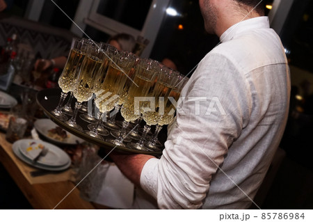 A waiter holding glasses with champagne served on a tablet A waiter holding glasses with champagne served on a tablet 85786984