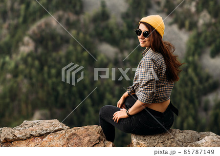 Portrait of a girl traveler in a yellow cap on the background of mountains. Portrait of a female tourist. The girl smiles and looks at the camera. Female tourist in the mountains. Copy space 85787149