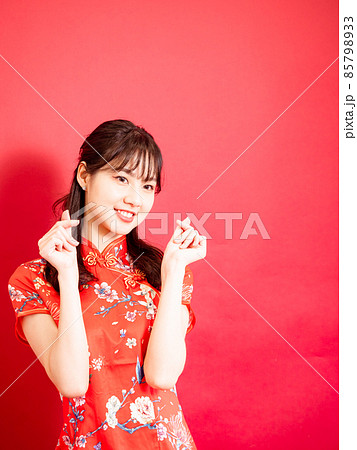 Young asian woman wear cheongsam showing mini heart sign isolated on red background. Young asian woman wear cheongsam showing mini heart sign isolated on red background. 85798933