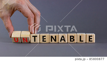 Tenable or untenable symbol. Businessman turns cubes and changes the word 'untenable' to 'tenable'. Beautiful grey table, grey background. Business, tenable or untenable concept, copy space. 85800877