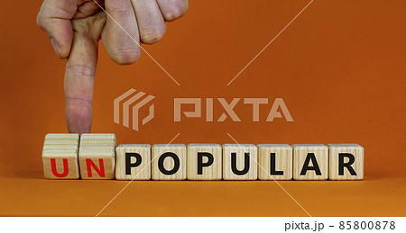 Popular or unpopular symbol. Businessman turns wooden cubes and changes the word unpopular to popular. Beautiful orange table, orange background. Popular or unpopular and business concept. Copy space. 85800878