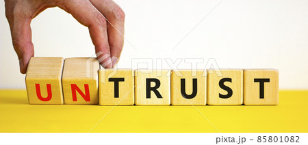 Untrust or trust symbol. Businessman turns wooden cubes, changes words 'untrust' to 'trust'. Beautiful yellow table, white background. Business and untrust or trust concept, copy space. Untrust or trust symbol. Businessman turns wooden cubes, changes words 'untrust' to 'trust'. Beautiful yellow table, white background. Business and untrust or trust concept, copy space. 85801082