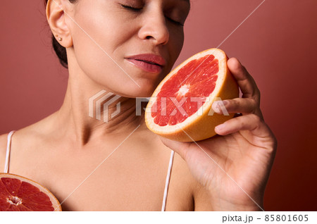 Middle aged beautiful woman with healthy glow perfect smooth skin holding grapefruit halves near her face. Natural cosmetics, skin care, wellness, beauty treatment, cosmetology concept. Close-up Middle aged beautiful woman with healthy glow perfect smooth skin holding grapefruit halves near her face. Natural cosmetics, skin care, wellness, beauty treatment, cosmetology concept. Close-up 85801605