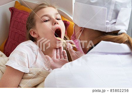 Children's doctor examining little girl's throat at home with a tongue depressor Children's doctor examining little girl's throat at home with a tongue depressor 85802256