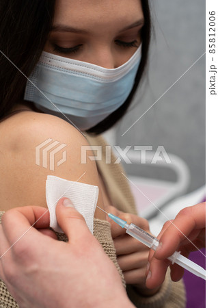 The doctor on duty sticks a needle into the arm to give the patient the vaccine. Up close, you can see a needle sticking into the human body. A sterile doctor's office. Men's hands. The COVID 85812006
