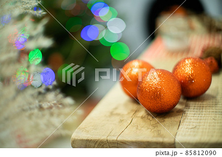 Gold-orange Christmas balls lie on a wooden board. Festive mood. Christmas time. Shiny Christmas tree lights in the background. 85812090