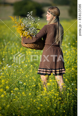 A young herbalist with a basket of herbs walks through a field full of flowering rapeseed. Goldenrod and wintercress. A young herbalist with a basket of herbs walks through a field full of flowering rapeseed. Goldenrod and wintercress. 85813586