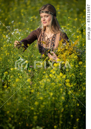 An herbalist checks her cultivated rapeseed fields. She holds a bouquet of herbs. An herbalist checks her cultivated rapeseed fields. She holds a bouquet of herbs. 85813697