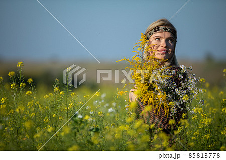 The herbalist stands in a cultivated field of rapeseed and looks up smiling. 85813778