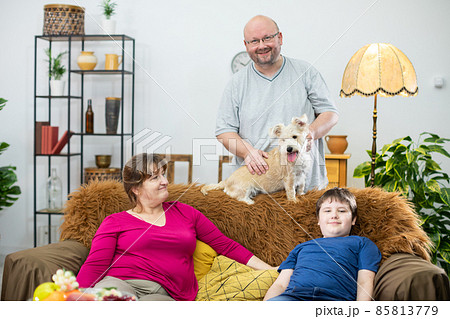 The father stands behind the sofa and strokes the shaggy dog the rest of the family watches all the fun. 85813779