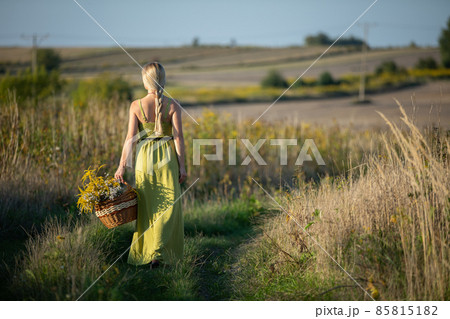 A young herbalist walks along a dirt road with a basket full of herbs. 85815182