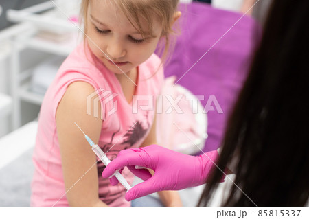 The doctor is giving a little girl an injection. The child stares in a choking bowl. Preventive vaccine for young children. 85815337