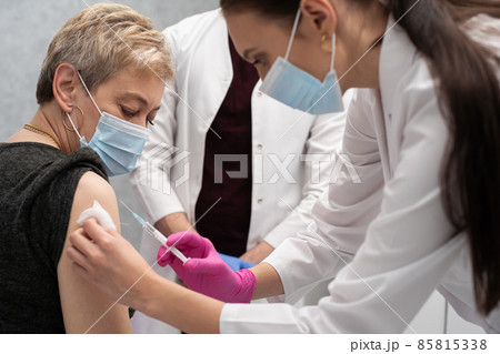 A nurse is making an vaccine to an elderly woman. The COVID vaccine19. A sterile doctor's office in a private clinic. A young medical intern looks at how to properly inject. 85815338