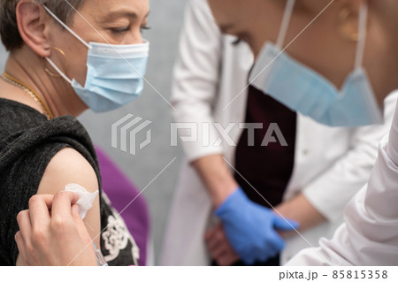 A nurse is making an vaccine to an elderly woman. The COVID vaccine19. A sterile doctor's office in a private clinic. A young medical intern looks at how to properly inject. 85815358