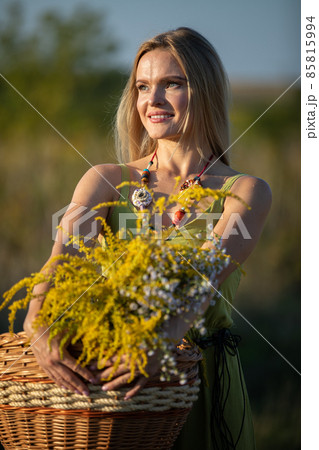 A young attractive herbalist holds a wicker basket of herbs. Goldenrod and common winterflower. 85815994